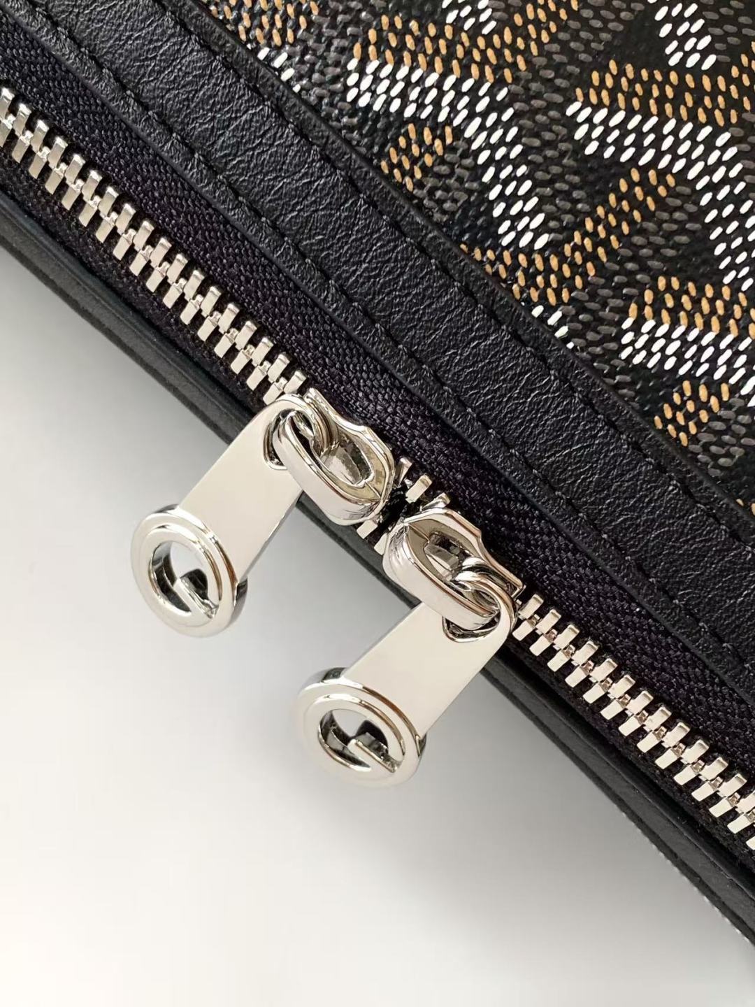 Goyard bag close-up of zipper hardware with metal rings on monogram fabric.