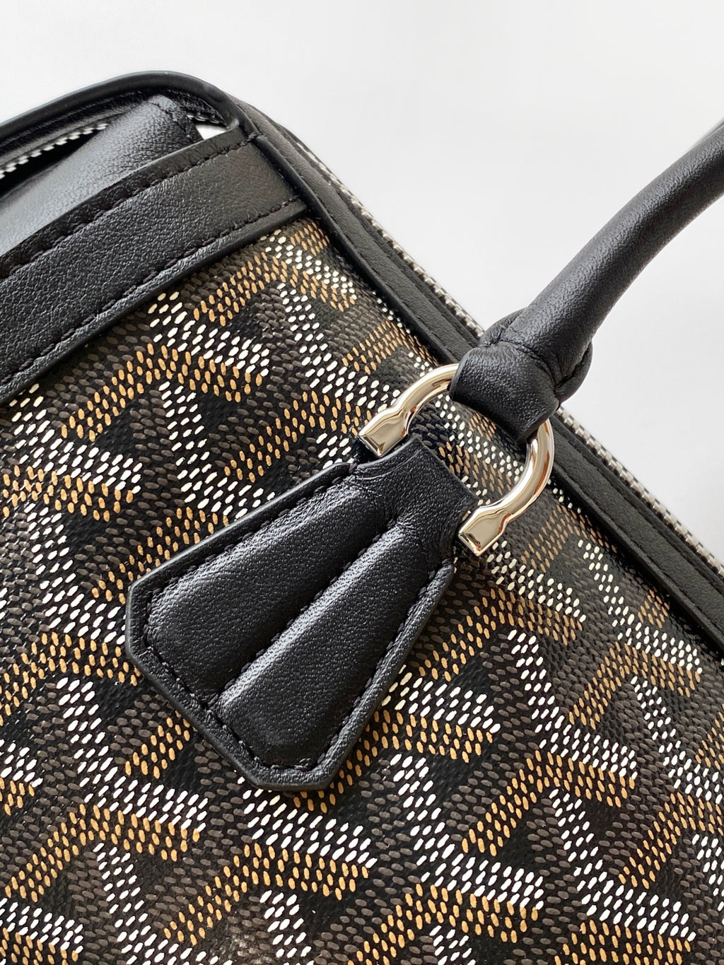 Goyard bag close-up of strap attachment and stitched leather pocket on monogram canvas.