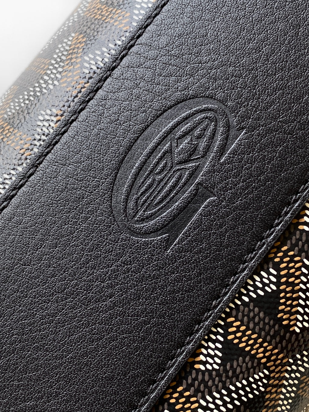 Goyard bag close-up of embossed logo on black leather trim and patterned fabric edge.