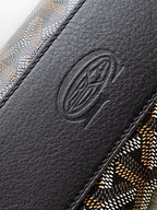 Goyard bag close-up of embossed logo on black leather trim and patterned fabric edge.