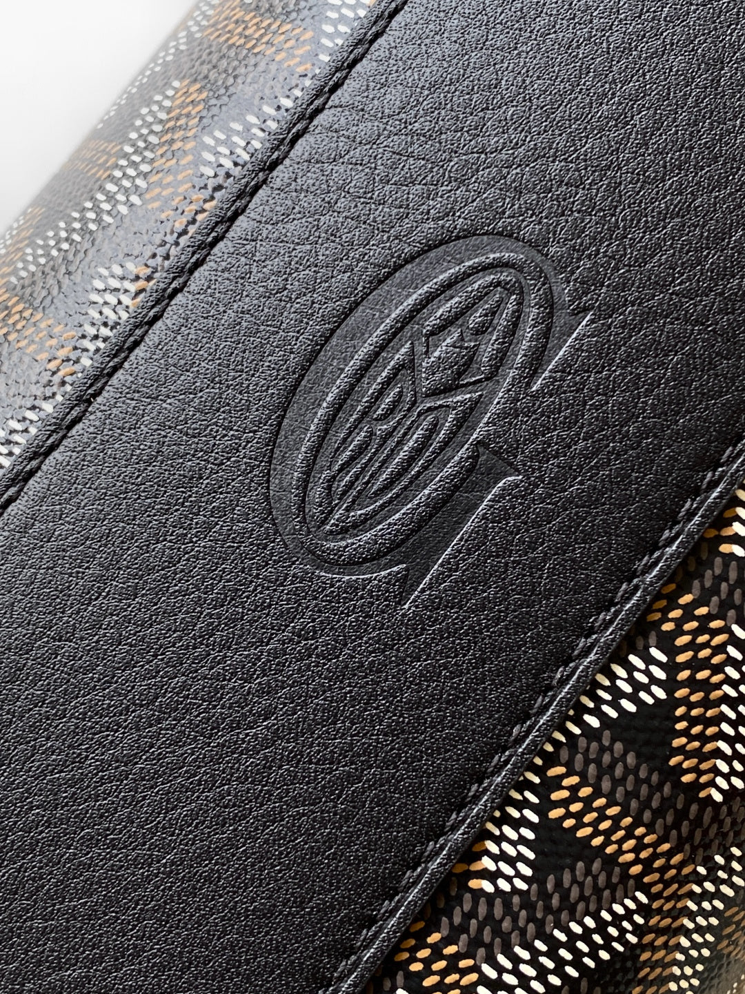 Goyard bag close-up of embossed logo on black leather trim and patterned fabric edge.