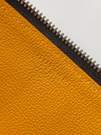 Goyard bag close-up of yellow leather panel with embossed logo and zipper teeth.