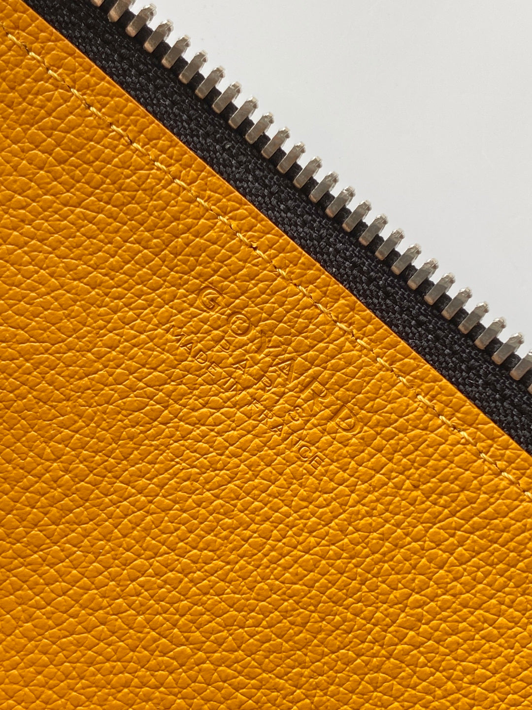 Goyard bag close-up of yellow leather panel with embossed logo and zipper teeth.