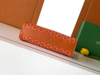 Orange patterned Goyard clutch-style bag with foldover front and short handle