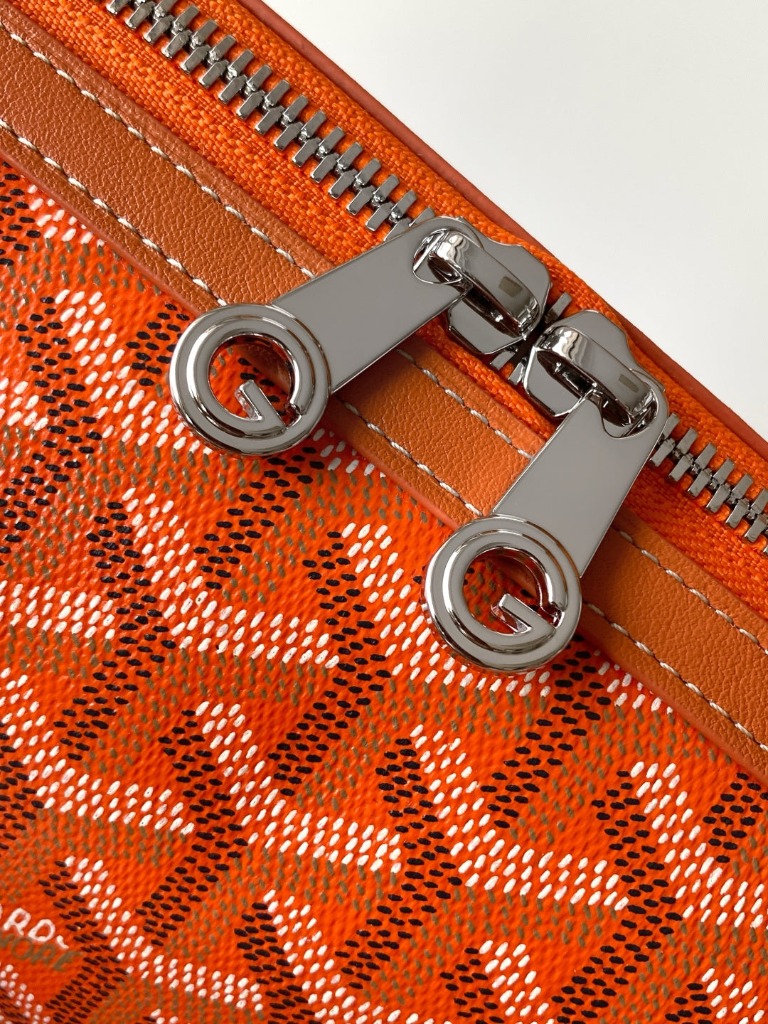 Orange patterned Goyard zipper with round metal rings on leather tabs