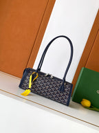 Goyard bag with navy patterned body, two top handles, yellow tag at zipper.