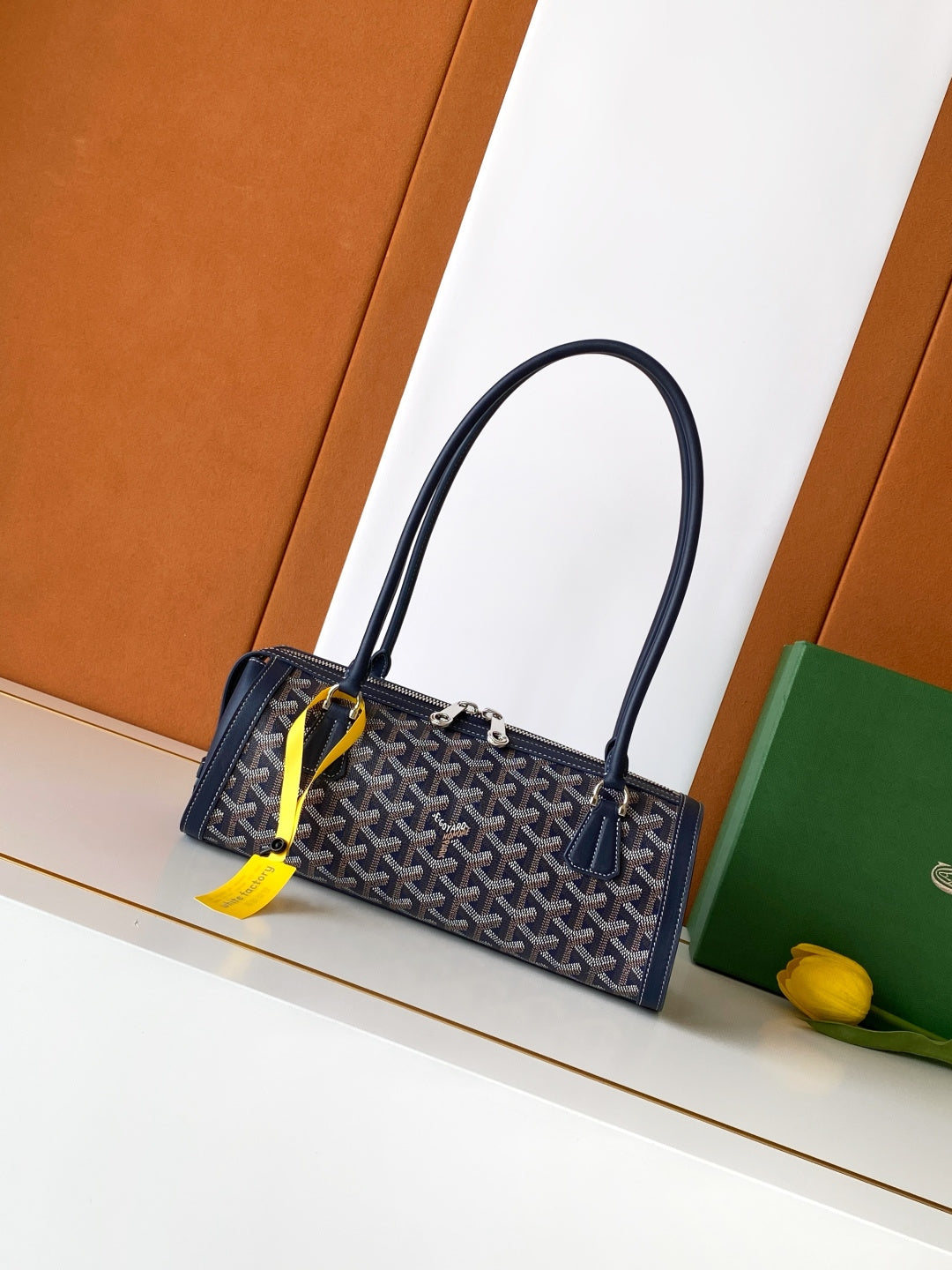 Goyard bag with navy patterned body, two top handles, yellow tag at zipper.