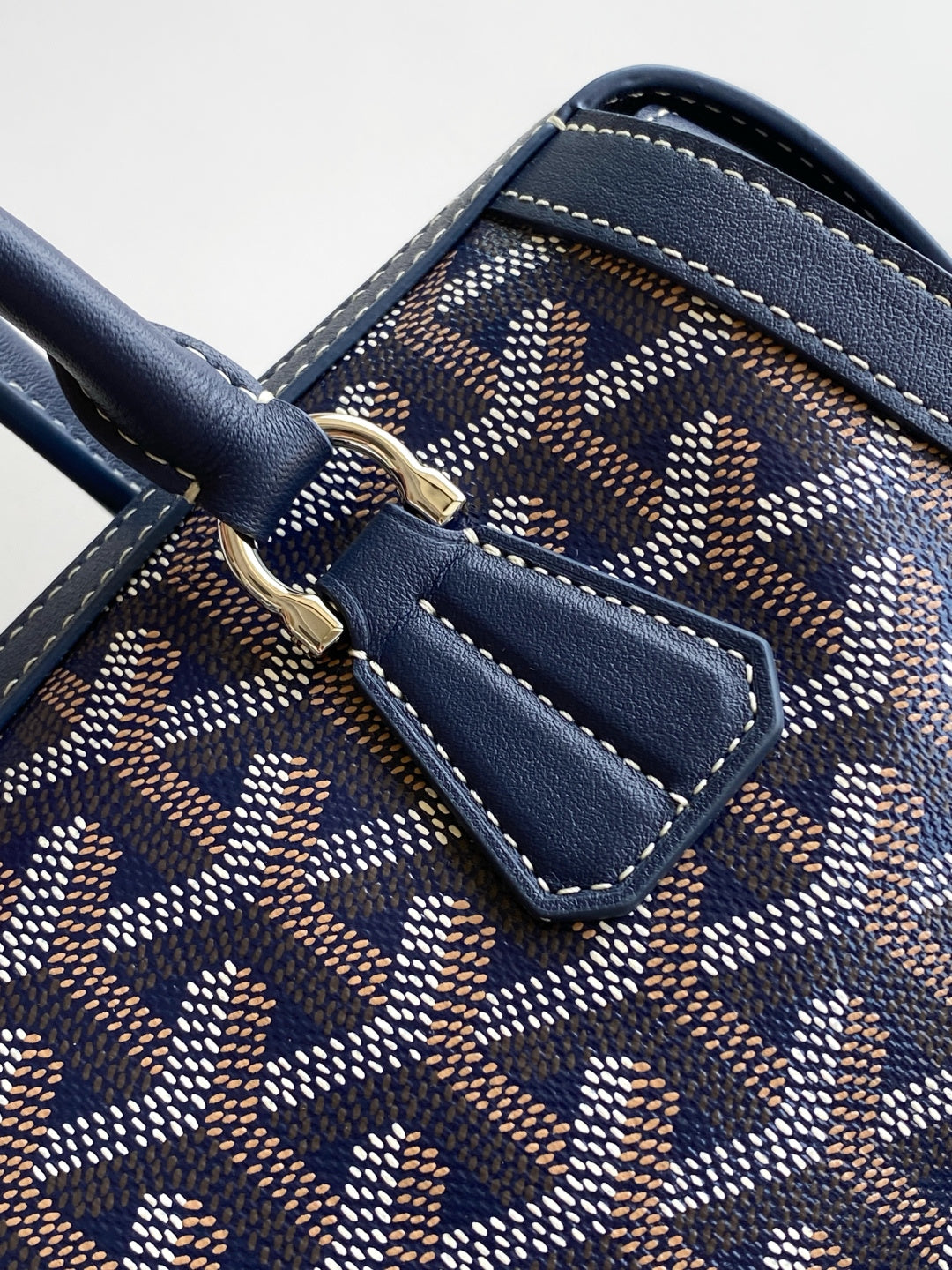 Goyard bag close-up of navy leather strap and patterned canvas with buckle tab.