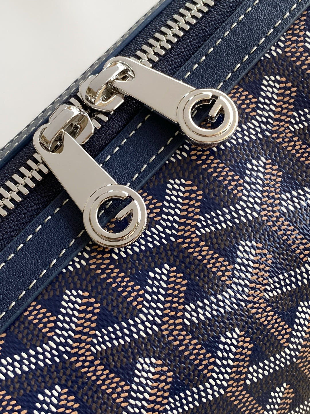 Goyard bag close-up of silver hardware and zipper pull on patterned fabric.