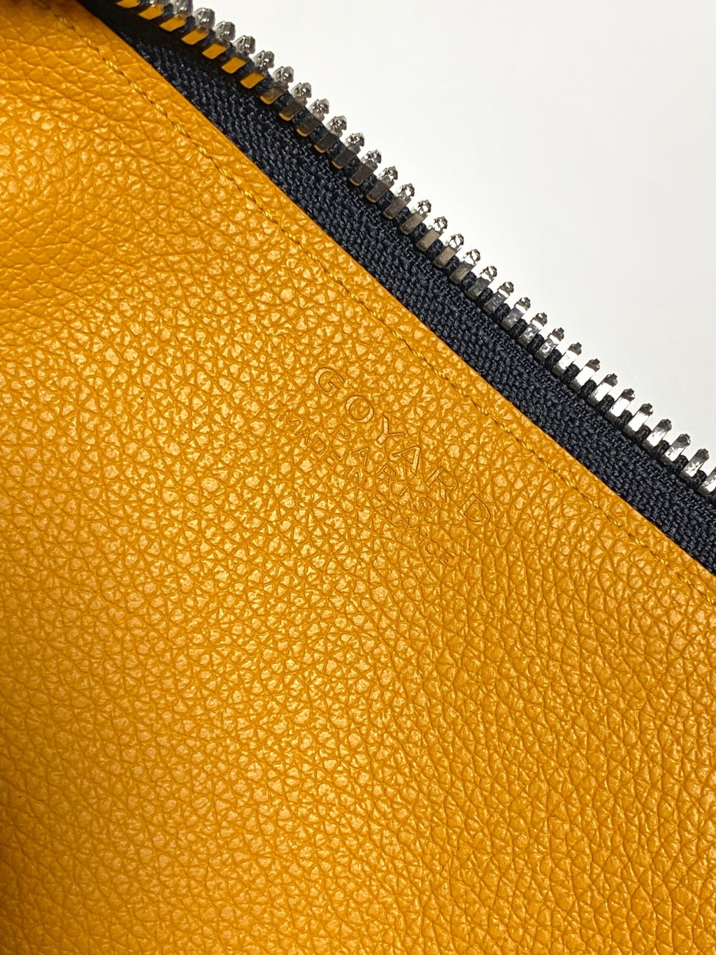 Goyard bag close-up of mustard leather interior edge with black zipper track.