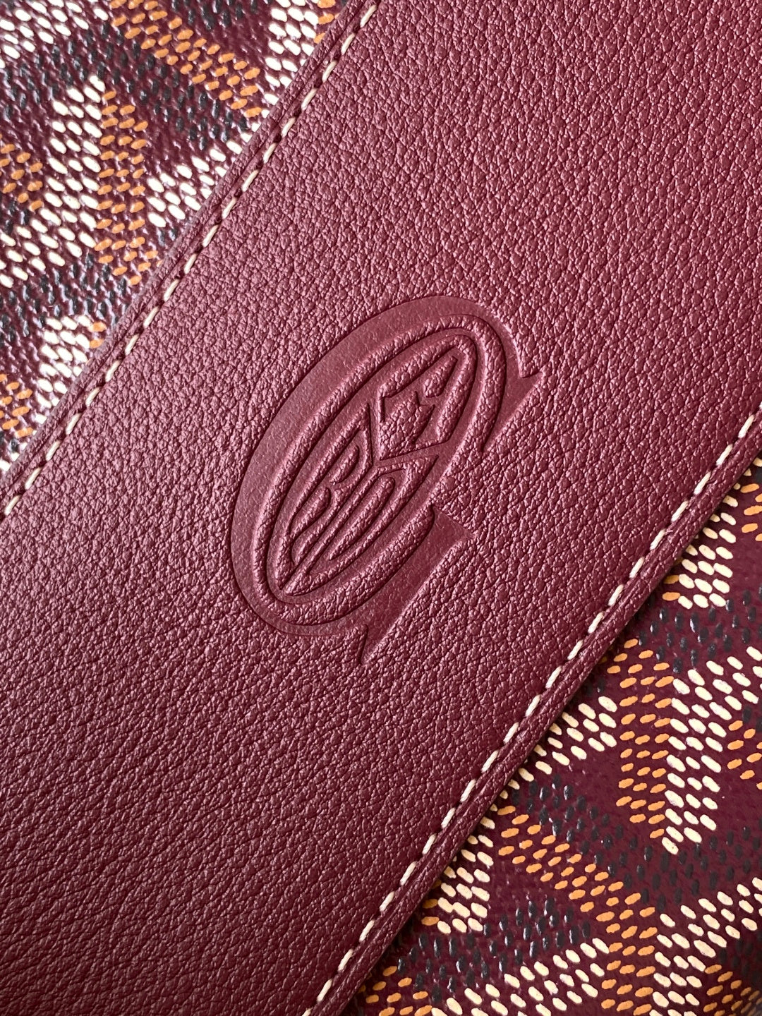 Burgundy leather panel with embossed oval logo and contrast stitching