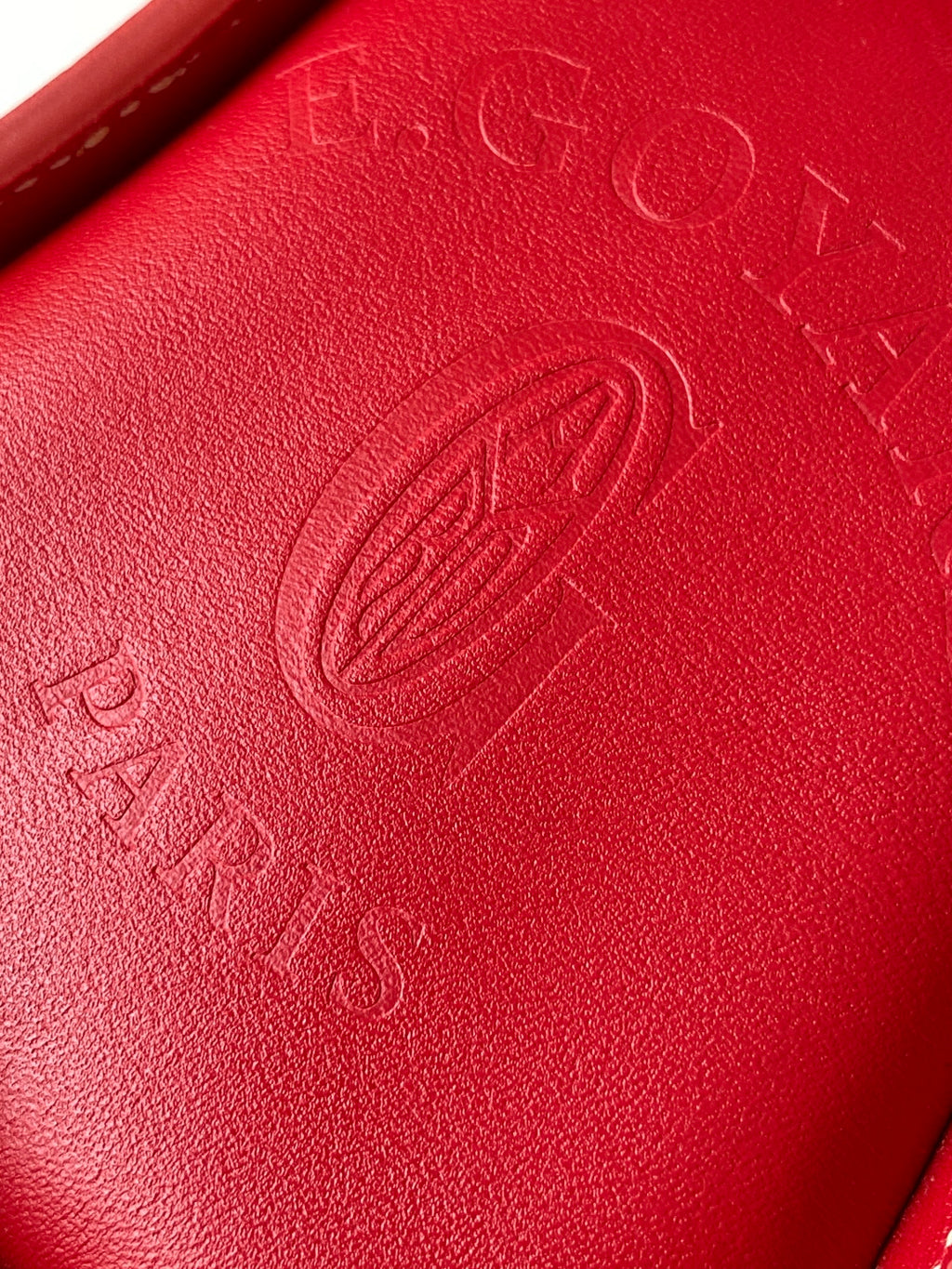 Red leather handbag surface with embossed logo and visible stitching detail