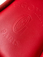 Red leather handbag surface with embossed logo and visible stitching detail