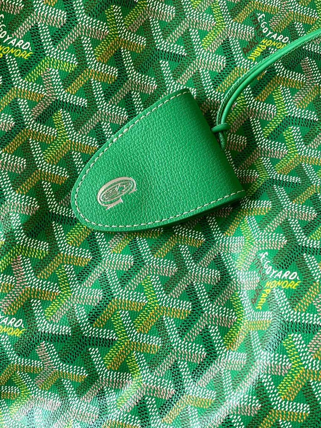 Goyard green leather tab with stitched emblem on patterned canvas tote