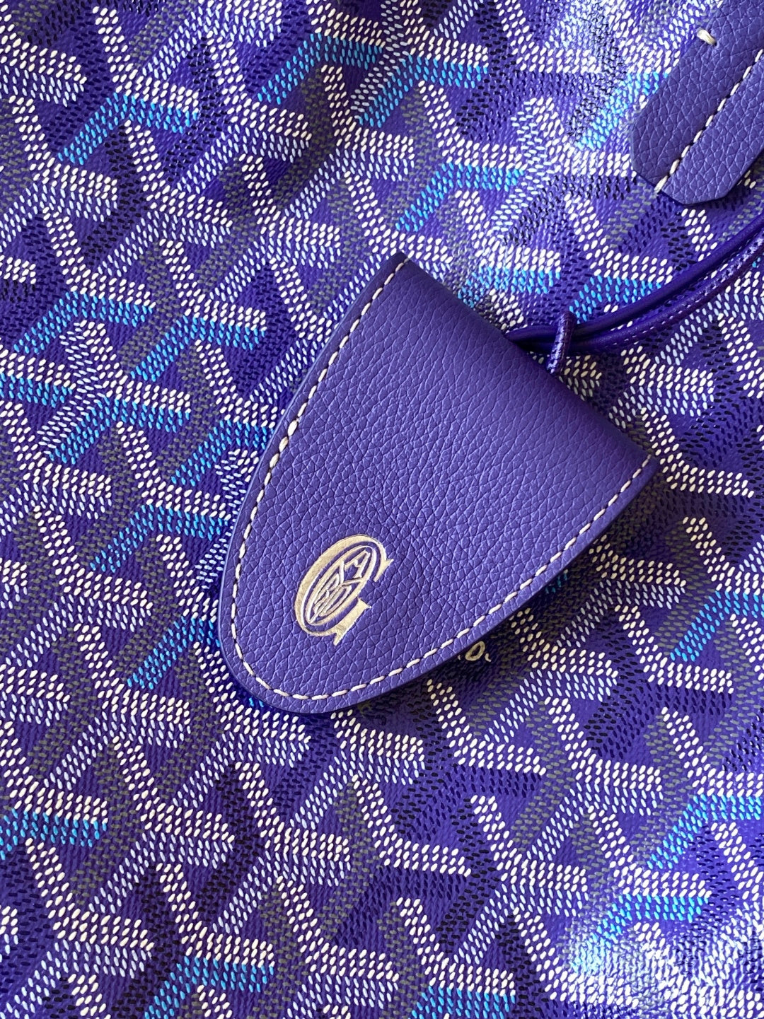 Blue patterned fabric tote bag with purple leather tab and circular logo emblem