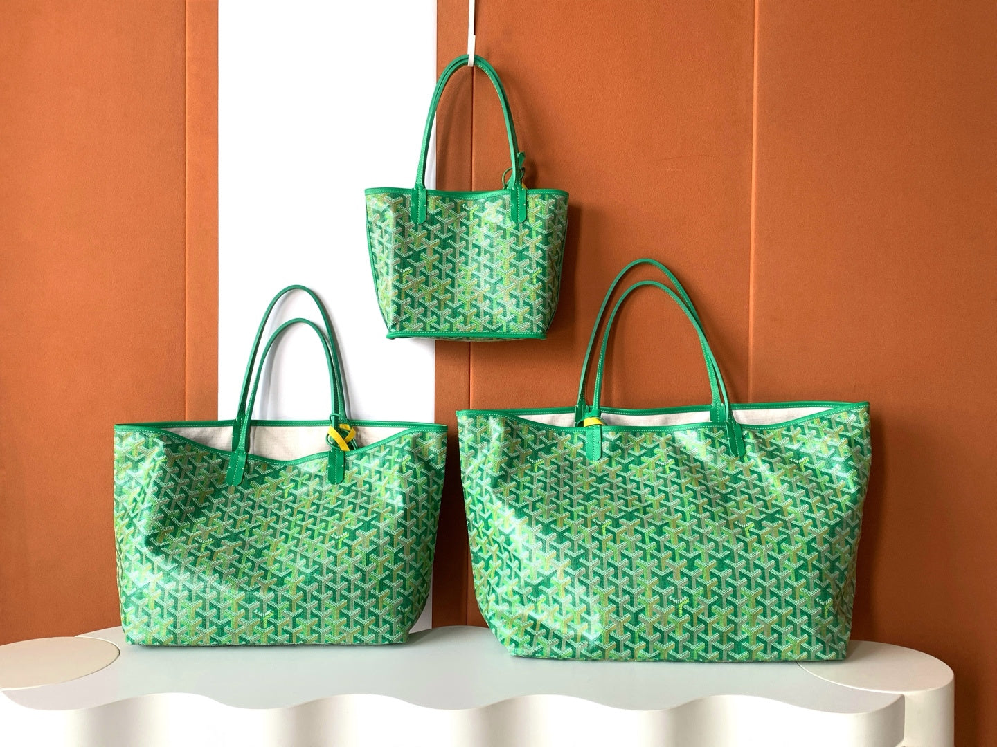 Three green patterned Goyard tote bags displayed together with handles