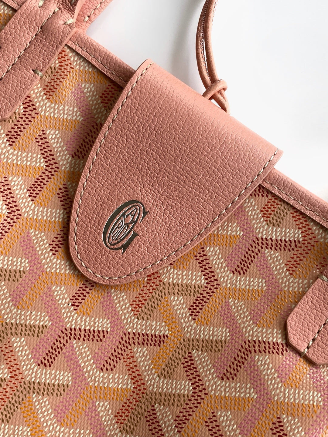 Pink patterned bag with leather tab and circular logo on the front pocket.