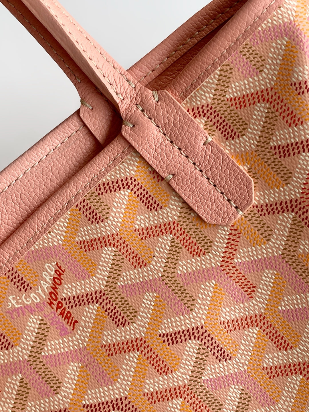 Pink patterned tote corner detail with leather strap and visible stitching.