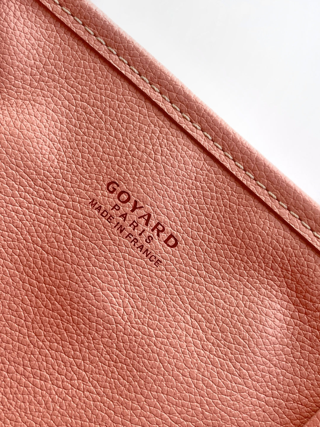 Pink pebbled leather tote with embossed “GOYARD” logo and text below.