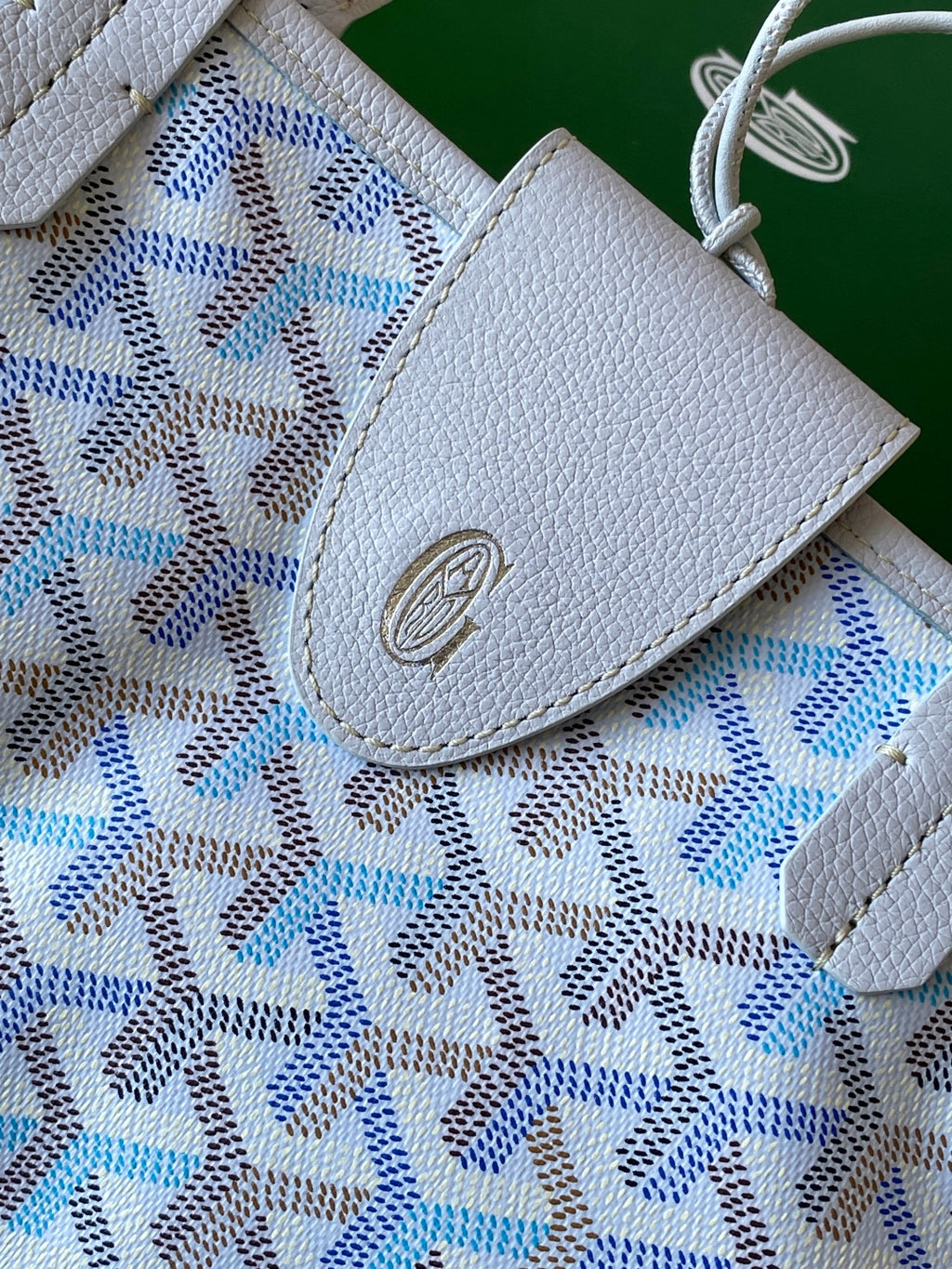 Light blue patterned tote bag flap with embossed logo medallion