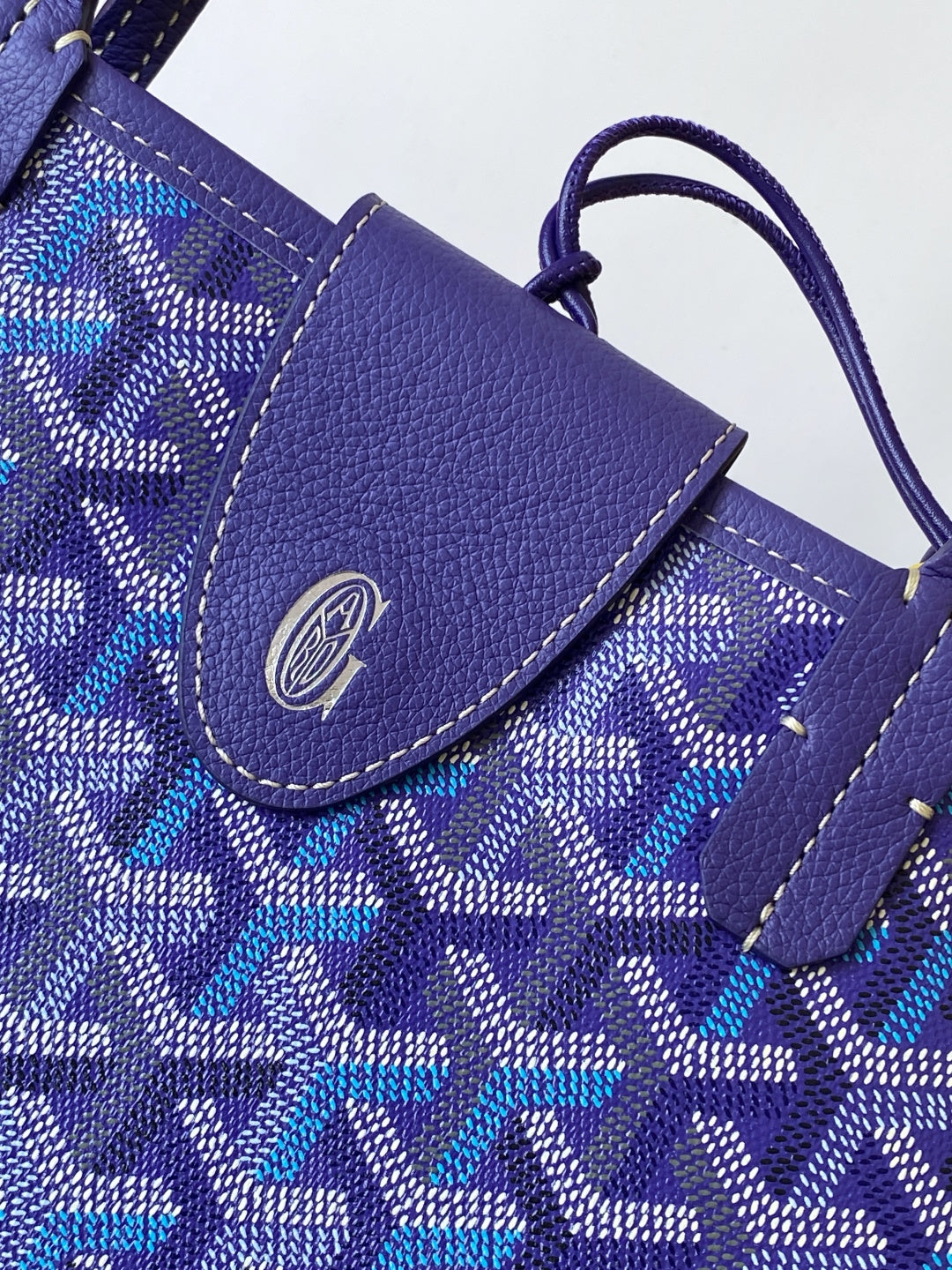 Goyard tote bag close-up, blue patterned flap with leather trim and stitched edge
