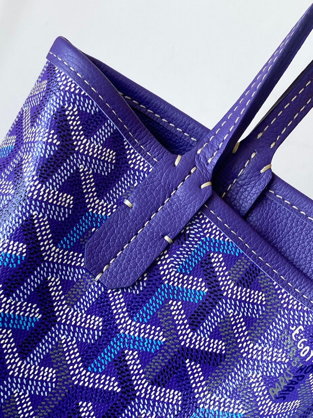 Goyard tote bag close-up, blue patterned panel with leather handle patch and contrast stitching