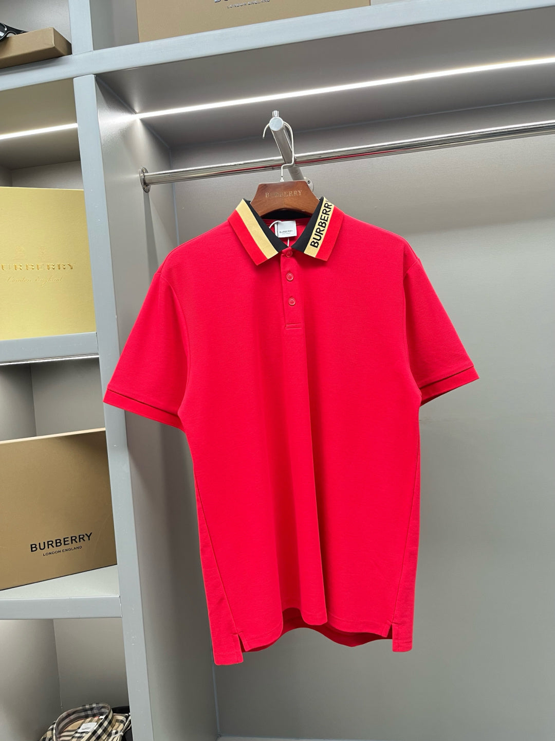 Red polo shirt with button placket and striped collar, on a hanger