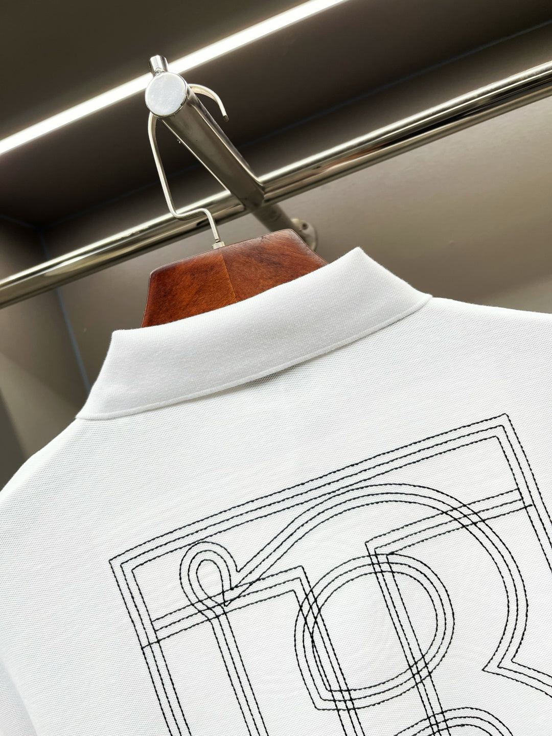 Close-up of white polo shirt back collar with large outlined monogram