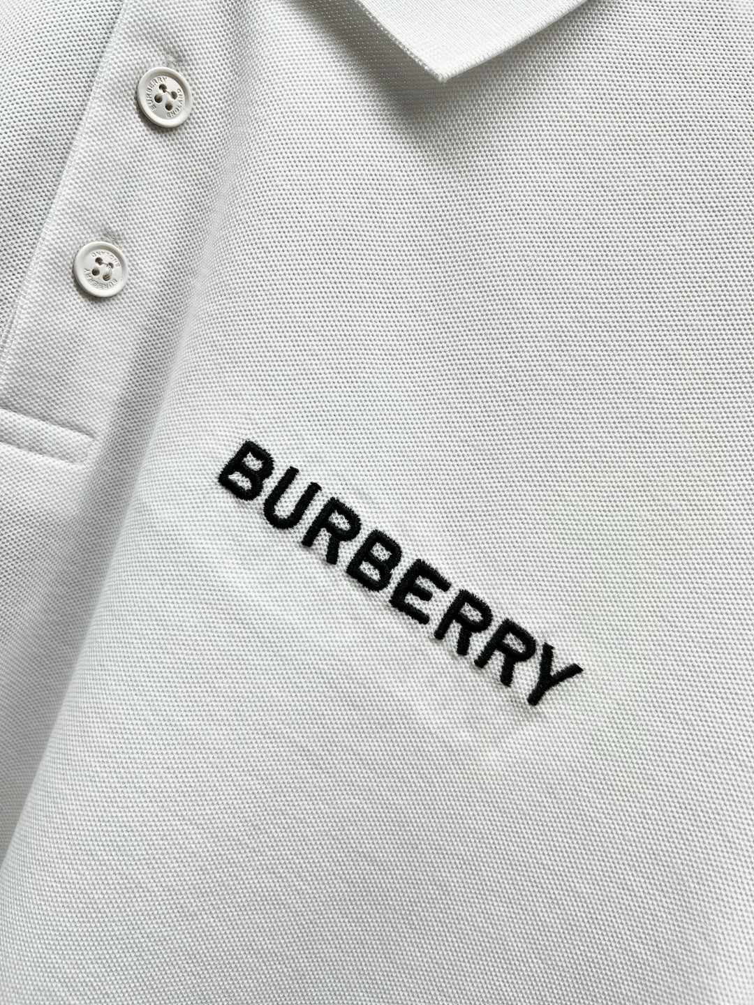Close-up of Burberry wordmark on white polo shirt fabric