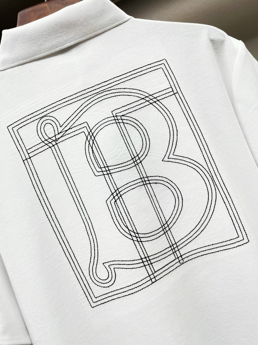 Close-up of white Burberry polo shirt back monogram graphic in outlined lines