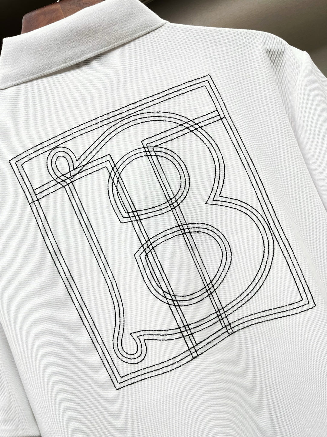 Close-up of white Burberry polo shirt back monogram graphic in outlined lines