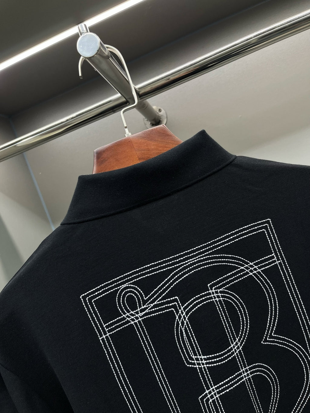 Black polo shirt back graphic with outlined lettering and number-style design.