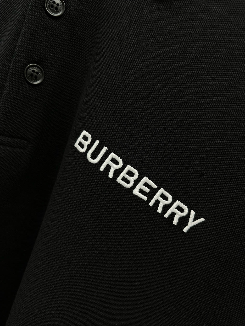 Burberry logo text on black polo shirt with button placket detail.