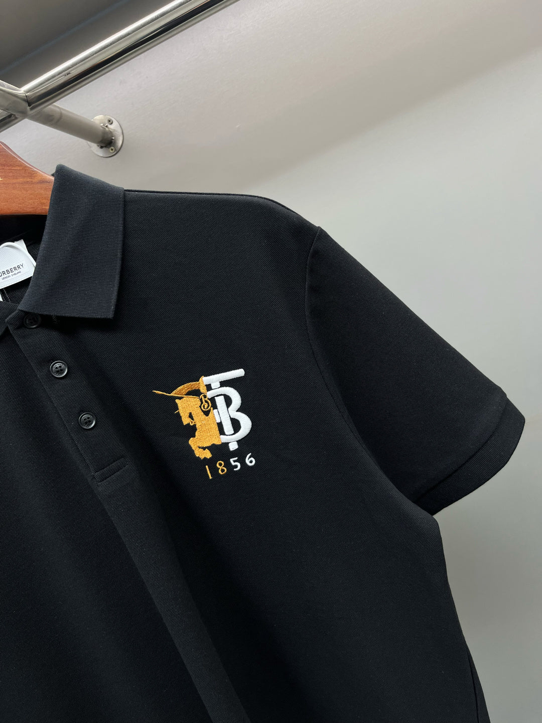 Black polo shirt with pointed collar and embroidered TB 1856 logo at left chest.