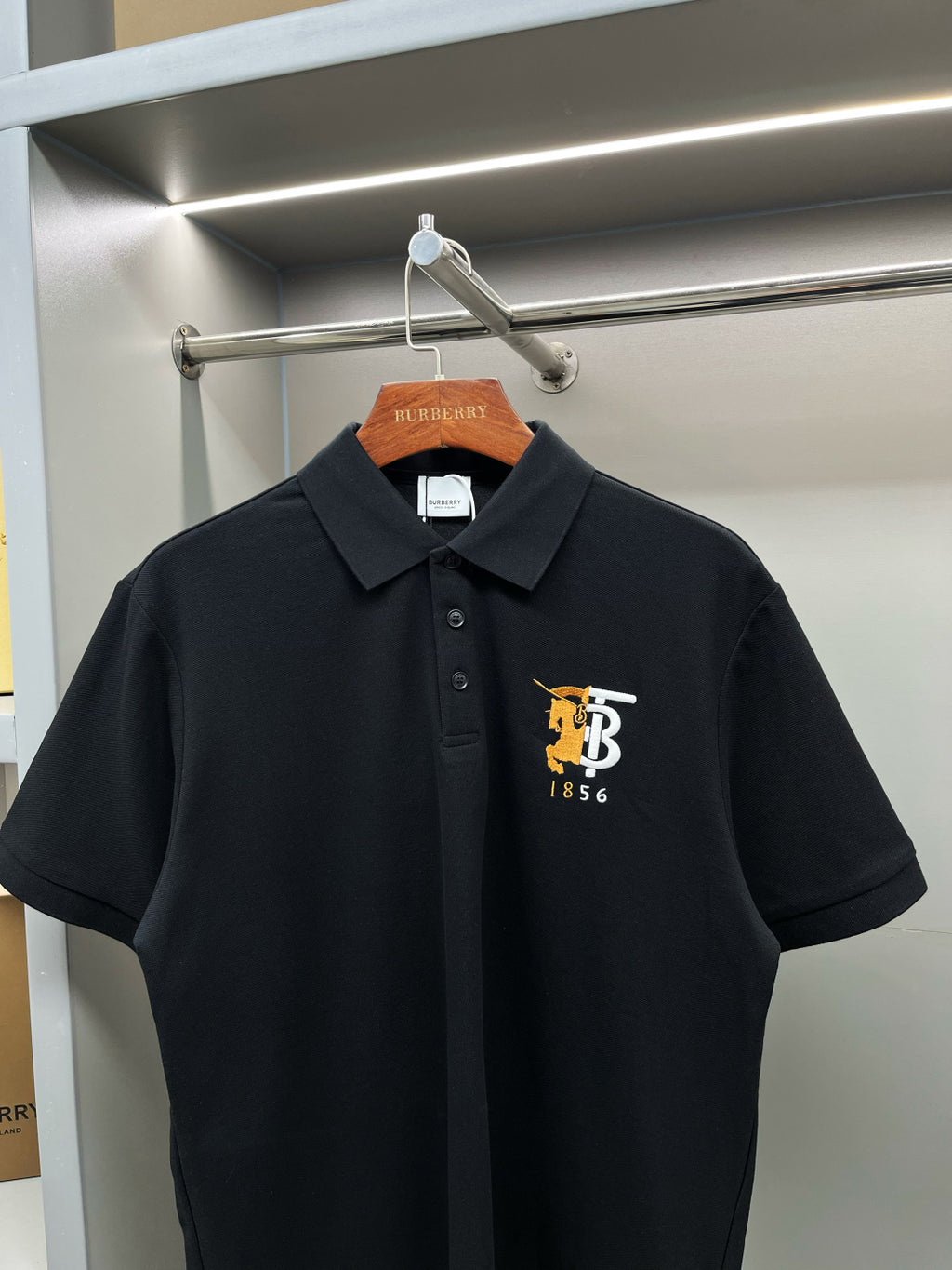 Black short-sleeve polo shirt with pointed collar and embroidered TB 1856 logo.