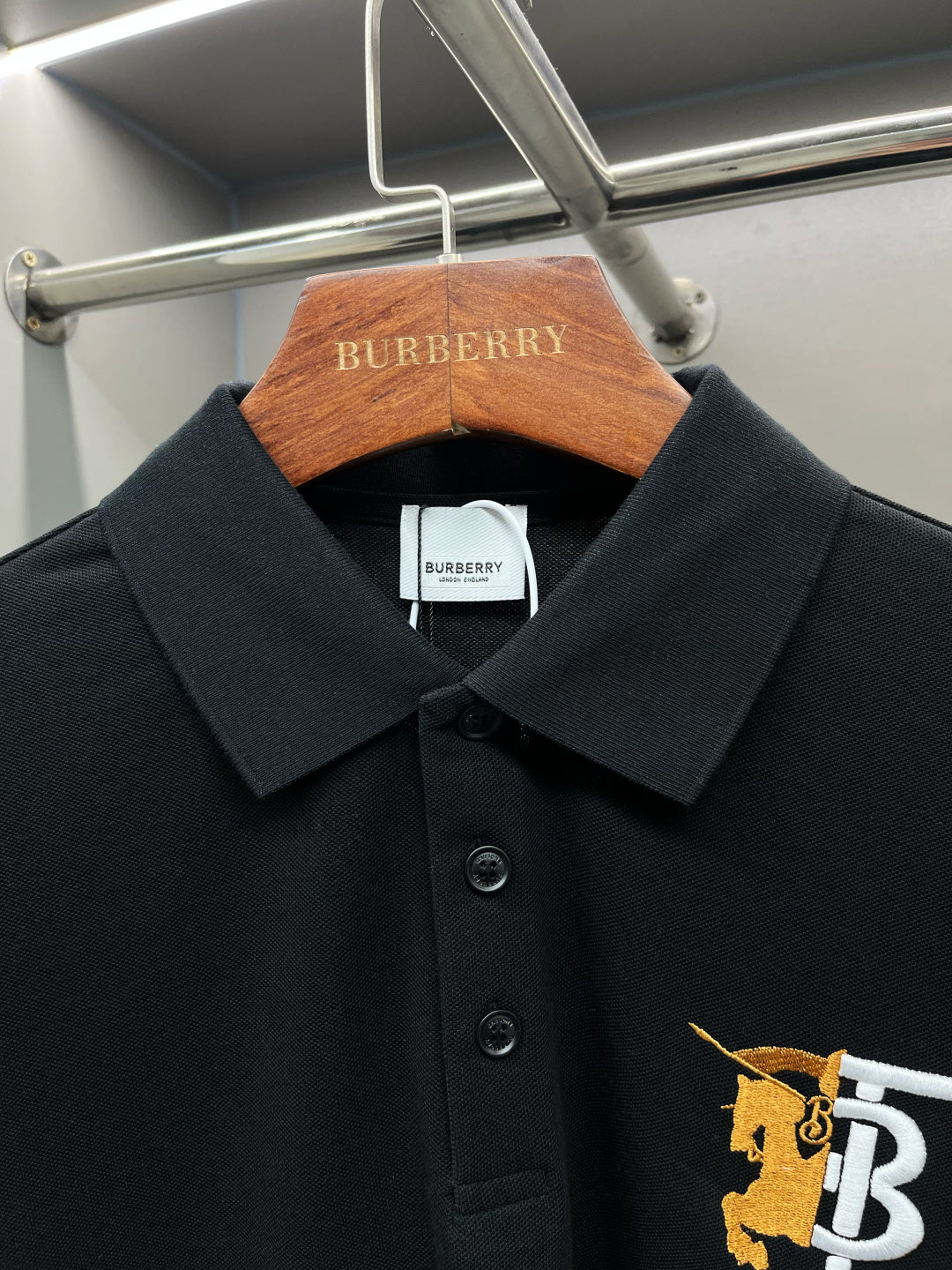 Black polo shirt with pointed collar, buttons, and embroidered TB 1856 on chest.