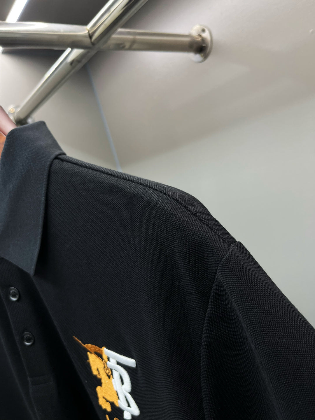 Side view of black polo shirt with embroidered TB 1856 logo at left chest.