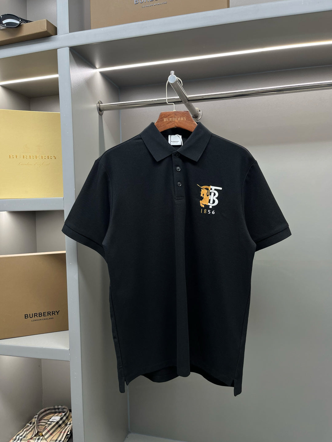 Black short-sleeve polo shirt with button placket and embroidered TB 1856 logo.
