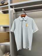 Light gray polo shirt with short sleeves, button placket, and yellow chest logo