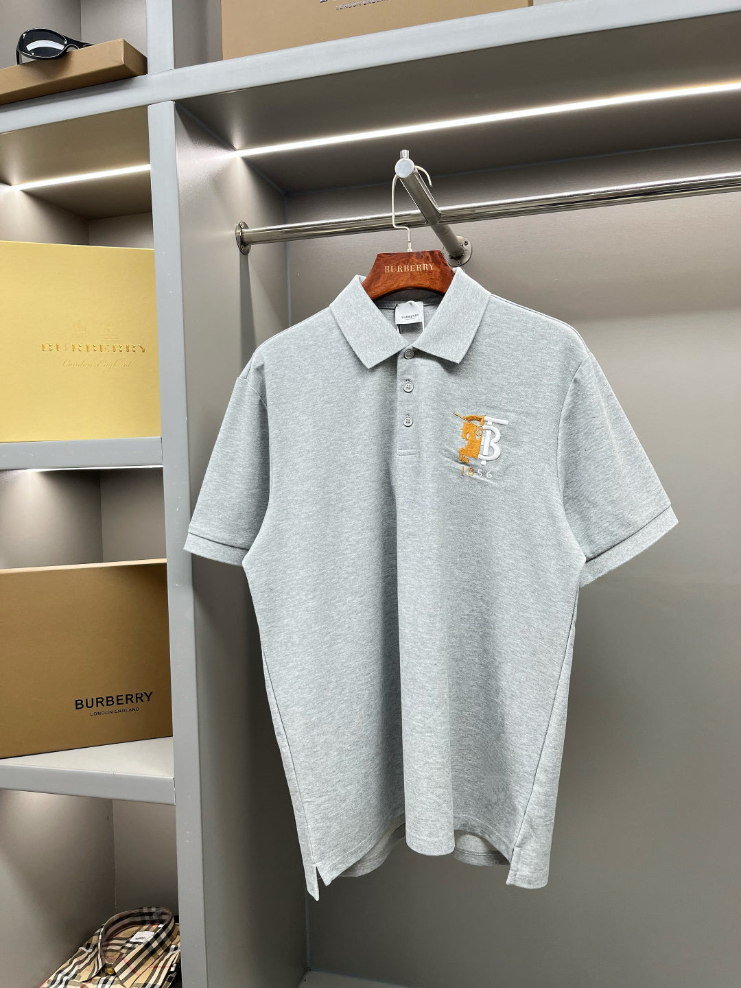 Light gray polo shirt with short sleeves, button placket, and yellow chest logo