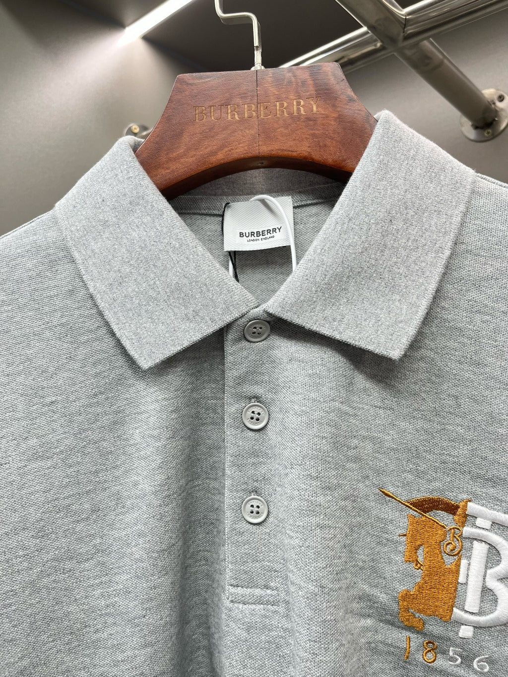 Light gray polo shirt collar with button placket and yellow logo embroidery