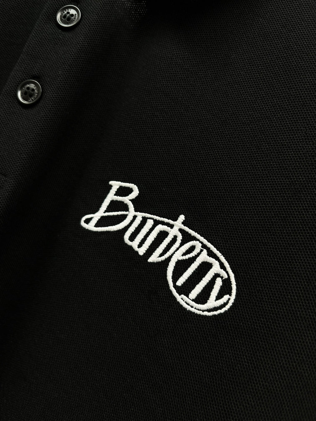 Black polo shirt fabric close-up with Burberry embroidered logo and button