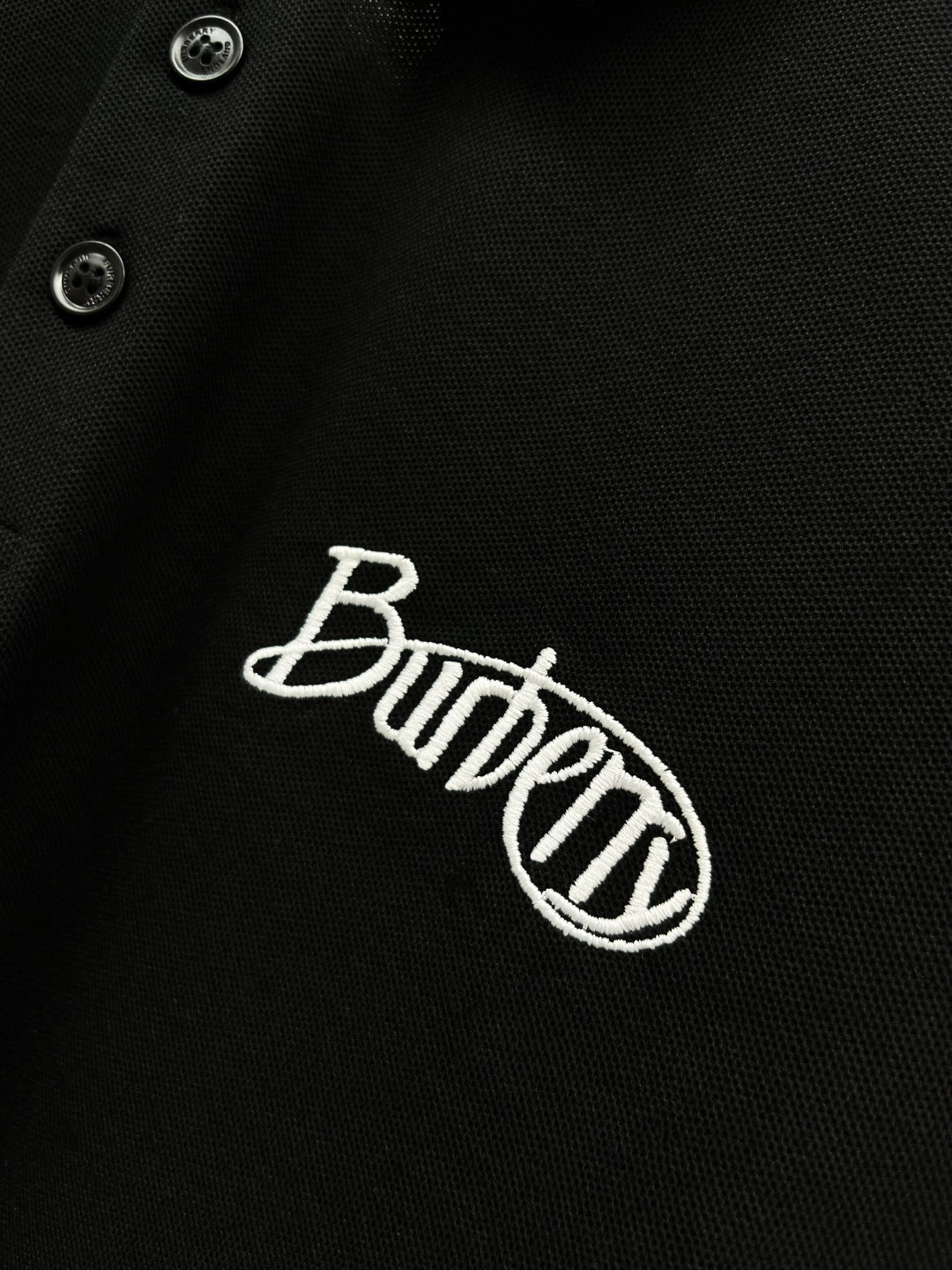 Black polo shirt fabric close-up with Burberry embroidered logo and button
