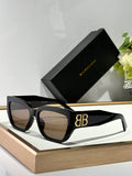 Balenciaga sunglasses with black frames, dark lenses, and gold B logo on arm.