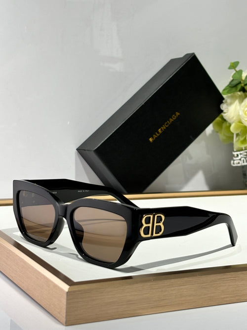 Balenciaga sunglasses with black frames, dark lenses, and gold B logo on arm.