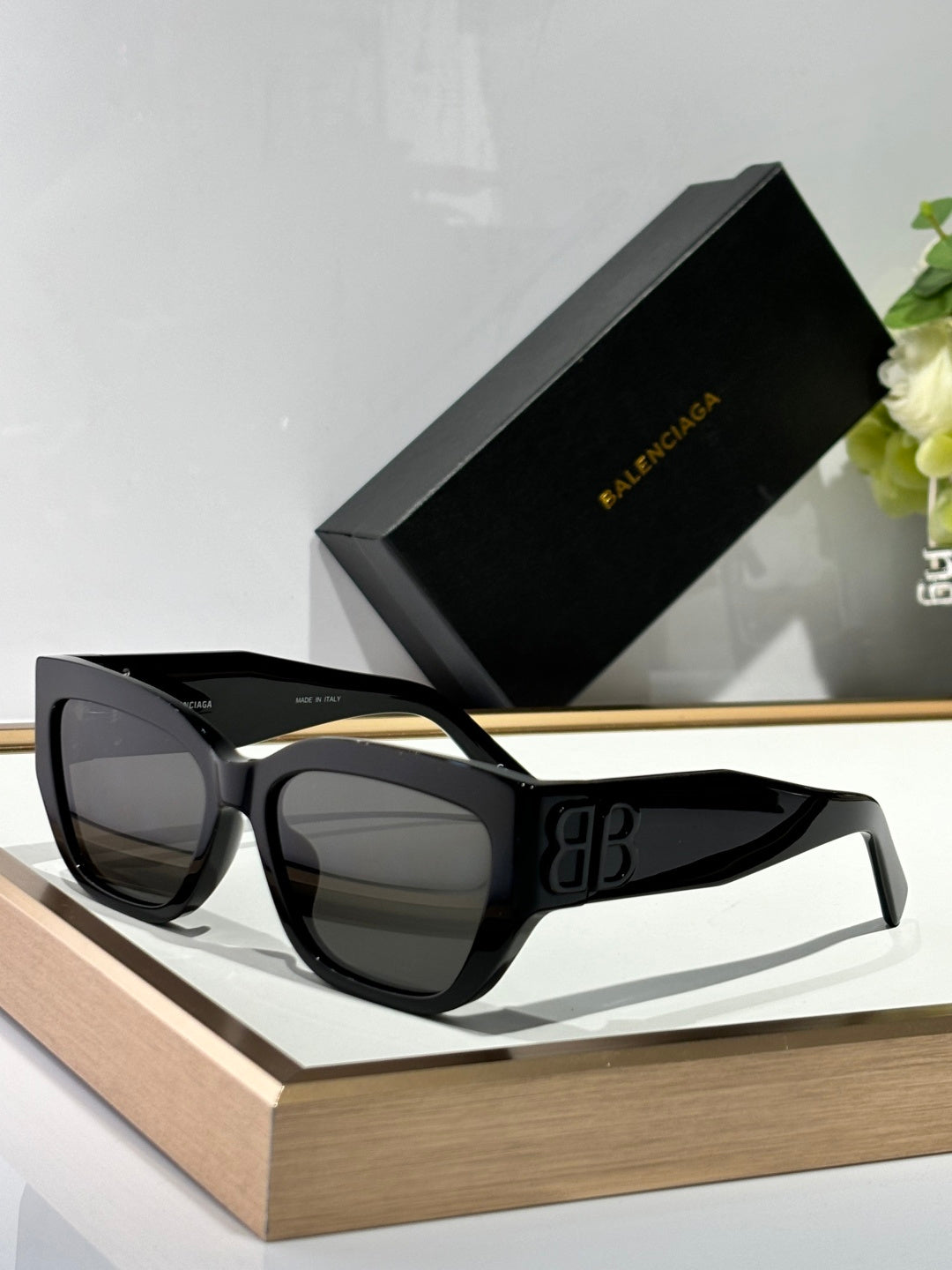 Balenciaga sunglasses with black frames and dark lenses, showing the gold B B emblem.