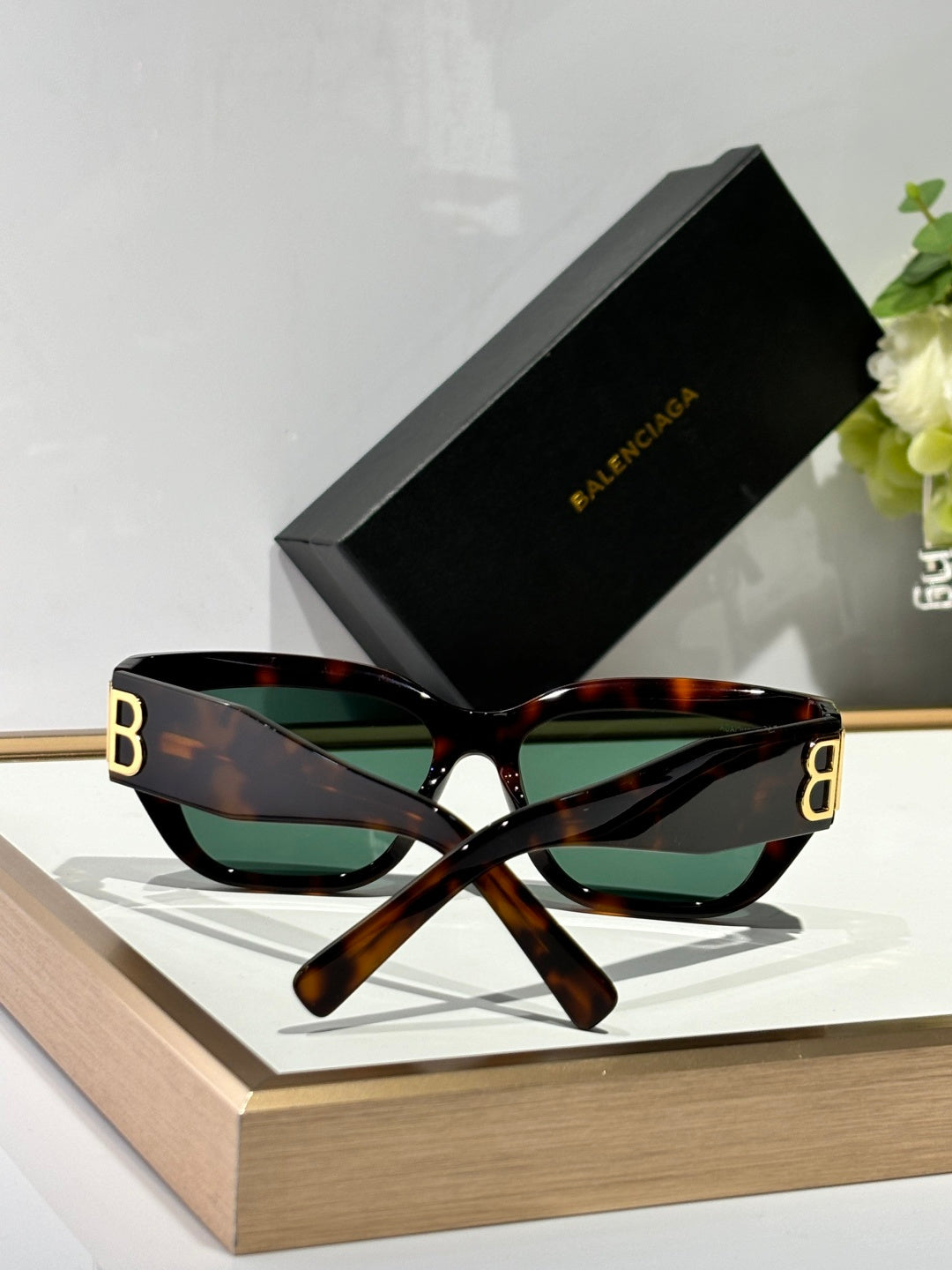 Balenciaga sunglasses with tortoiseshell frames, green-tinted lenses, and gold B B detail.