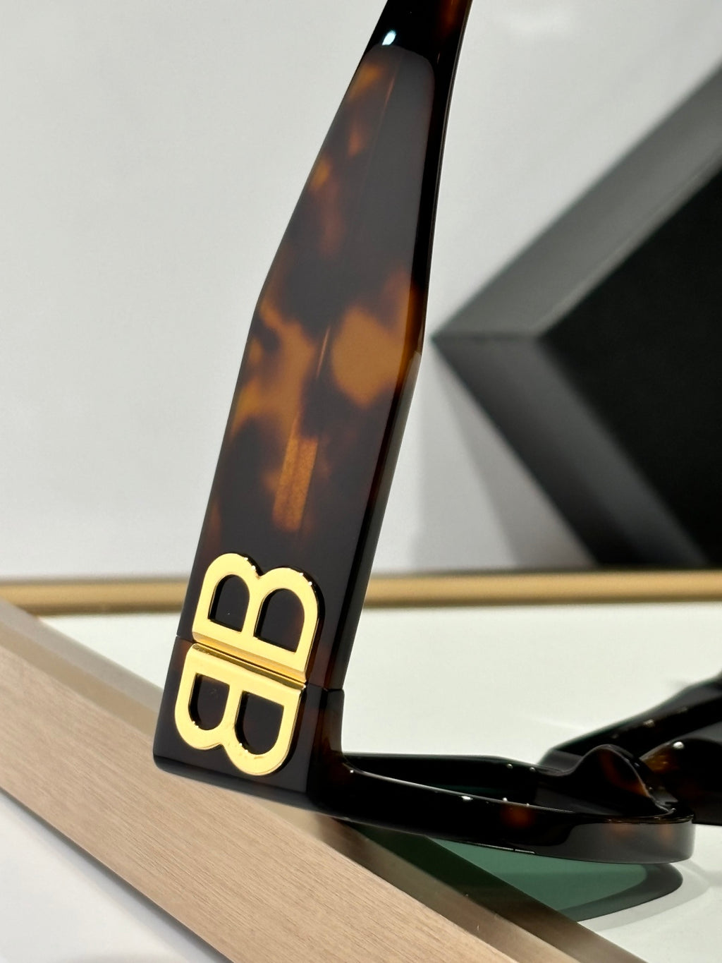 Balenciaga sunglasses temple close-up in tortoiseshell with gold B logo and lens edge.