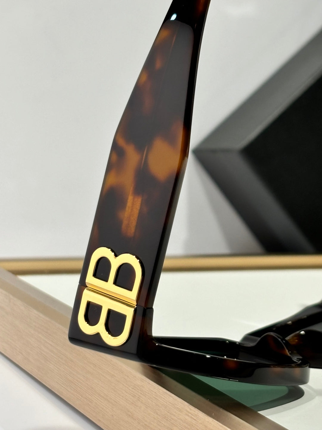 Balenciaga sunglasses temple close-up in tortoiseshell with gold B logo and lens edge.