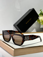 Balenciaga sunglasses with tortoiseshell frames and dark lenses, featuring a gold B B emblem.